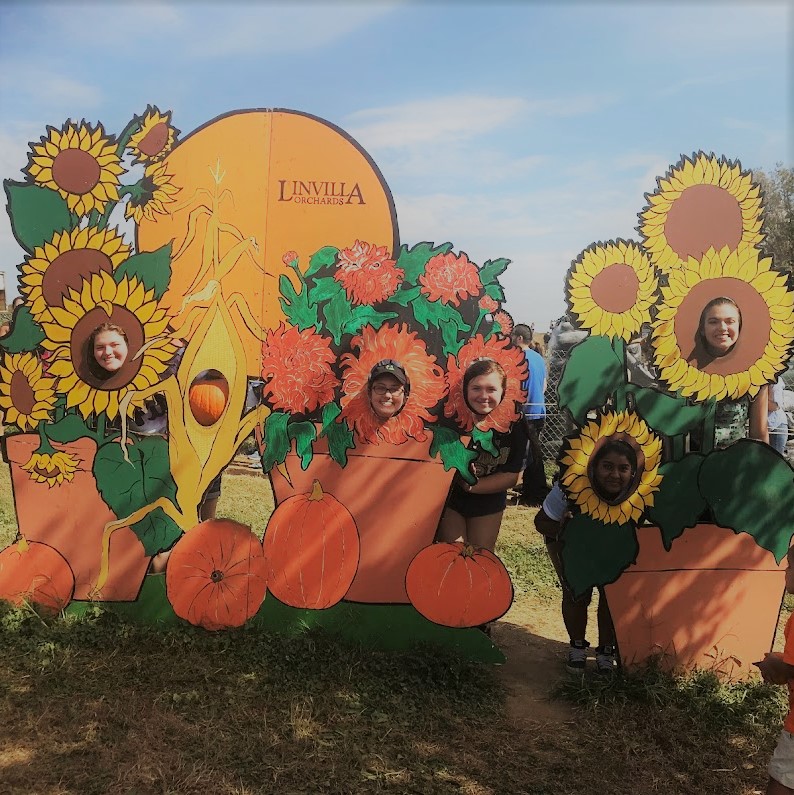 A group of four teenagers behind a large pumpkin sign reading Linvilla Orchard.