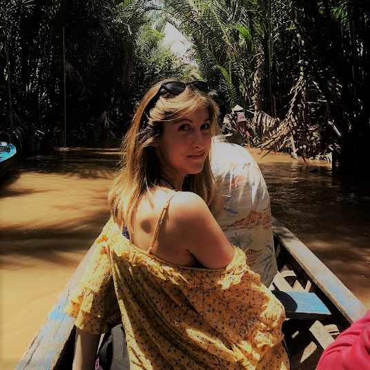 A young blonde woman in a boat looking back over her shoulder at the camera.