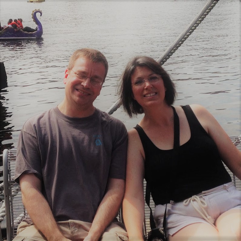 A man and a woman sitting on a bench, smiling and leaning towards each other.