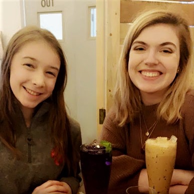 Two young women at a table smiling at the camera.